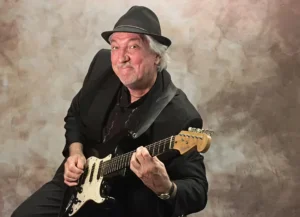 Man playing electric guitar, wearing a hat.